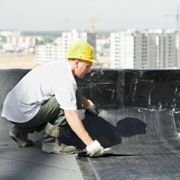 Roofing Guys Brisbane specialist applying waterproofing membrane on a commercial rooftop, part of routine strata and commercial roof maintenance services Roofing Guys Brisbane specialist applying waterproofing membrane on a commercial rooftop, part of routine strata and commercial roof maintenance services