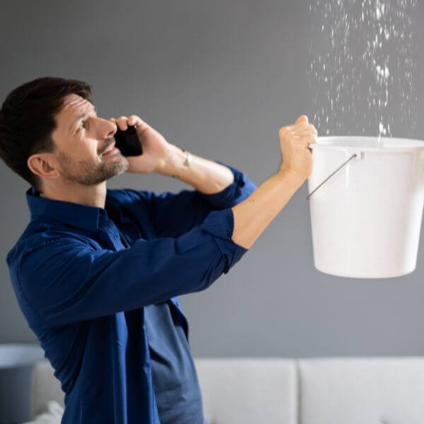 Worried business owner catching water from a ceiling leak with a bucket while calling Roofing Guys Brisbane, experts in fast commercial roof leak detection and repairs across Brisbane Worried business owner catching water from a ceiling leak with a bucket while calling Roofing Guys Brisbane, experts in fast commercial roof leak detection and repairs across Brisbane